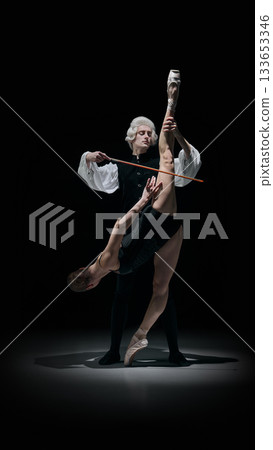 Classical conductor elevating dancer into sculptural instrument-like pose in dramatic theatre scene Classical conductor elevating dancer into sculptural instrument-like pose in dramatic theatre scene 133653346