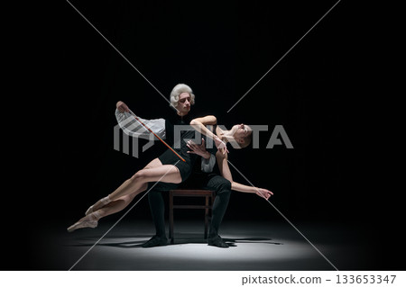 Classical conductor shaping dancer body like a musical instrument on dark stage 133653347
