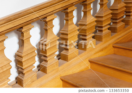 Warm wooden balusters form elegant repeating pattern along staircase in soft daylight. Smooth surfaces and crafted details create refined atmosphere with gentle shadows Warm wooden balusters form elegant repeating pattern along staircase in soft daylight. Smooth surfaces and crafted details create refined atmosphere with gentle shadows 133653350