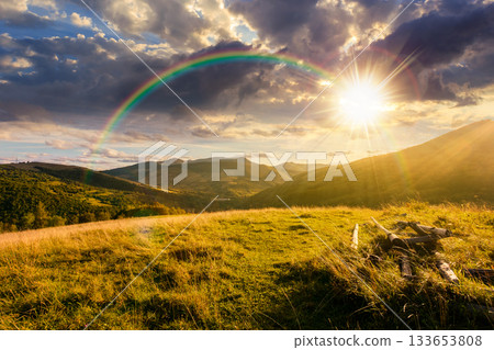beautiful countryside at sunset. wonderful summertime landscape in mountains in evening light. scenic view of grassy field and rolling hills. rural scenery storytelling image under the rainbow 133653808