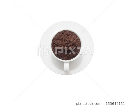 White cup on a white saucer filled with ground coffee, isolated on white background, top view. Minimalist composition for concepts of caffeine, freshness, and morning energy. White cup on a white saucer filled with ground coffee, isolated on white background, top view. Minimalist composition for concepts of caffeine, freshness, and morning energy. 133654131