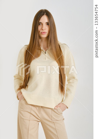 A woman in a cream sweater poses with her hands in pockets of beige pants A woman in a cream sweater poses with her hands in pockets of beige pants 133654754
