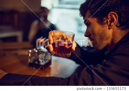 Man examining whiskey glass with bottle on table 133655173