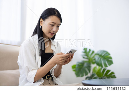 Smiling woman using a smartphone while relaxing on the sofa Smiling woman using a smartphone while relaxing on the sofa 133655182