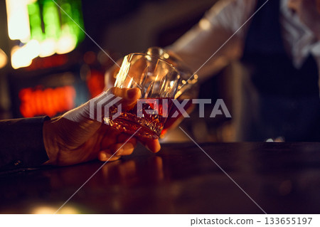 Close-up hands clinking whiskey glasses in dim bar. 133655197