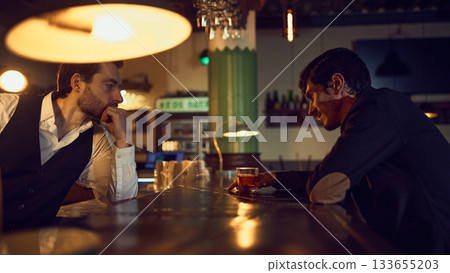 Bartender talking with customer holding drink at bar table 133655203