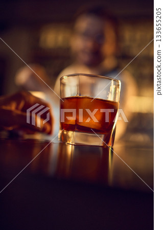 Low angle close-up of amber drink with ice on bar surface 133655205