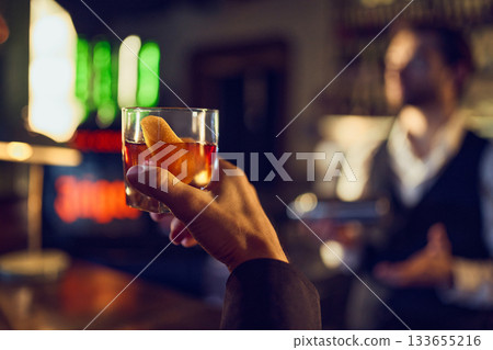 Hand lifting cocktail with citrus twist under neon bar lights Hand lifting cocktail with citrus twist under neon bar lights 133655216