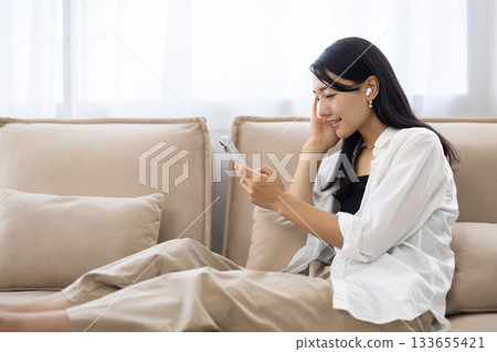Smiling woman wearing wireless earphones and looking at her smartphone 133655421
