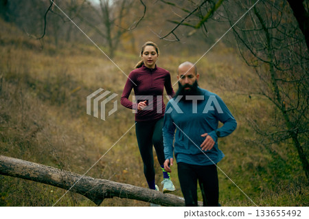 Couple running past fallen log during relaxed forest training 133655492