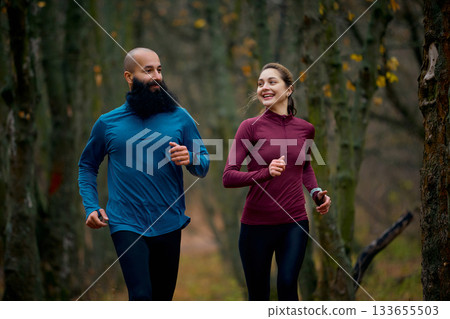 Smiling runners enjoying relaxed pace on forest trail Smiling runners enjoying relaxed pace on forest trail 133655503
