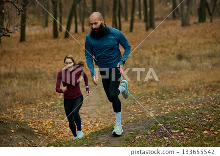 Runners powering uphill on forest trail during intense autumn training Runners powering uphill on forest trail during intense autumn training 133655542