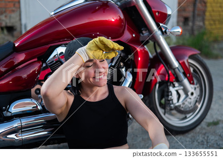 Brunette woman repairs a red motorcycle. Brunette woman repairs a red motorcycle. 133655551