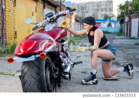 Brunette woman in denim shorts repairs a red motorcycle.  133655553