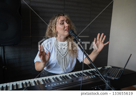 Caucasian woman singing into microphone and playing synthesizer and recording herself on laptop.  133655619