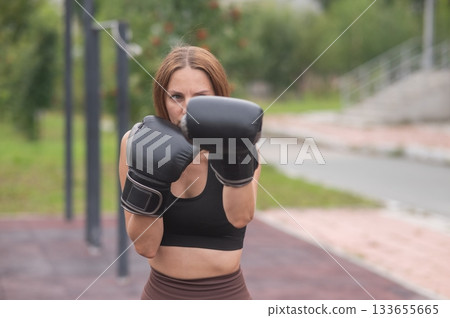 A Caucasian woman practices boxing outdoors.  133655665
