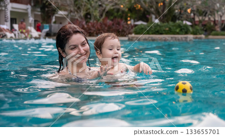 Caucasian woman holds son while swimming in pool on vacation. Caucasian woman holds son while swimming in pool on vacation. 133655701