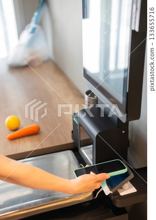 A woman pays using her smartphone at a self-checkout. A woman pays using her smartphone at a self-checkout. 133655716