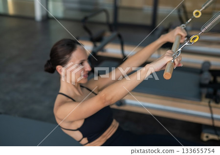 Caucasian woman doing exercises on reformer machine. Caucasian woman doing exercises on reformer machine. 133655754