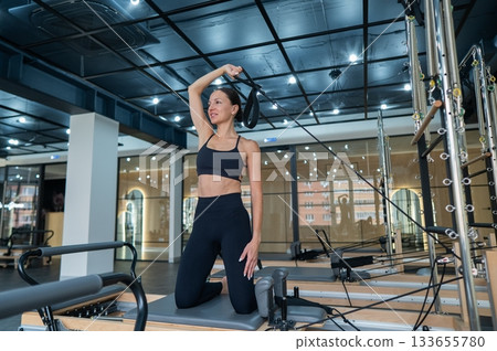 Caucasian woman doing exercises on reformer machine. Caucasian woman doing exercises on reformer machine. 133655780