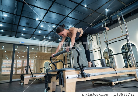 Caucasian woman doing exercises on reformer machine. Caucasian woman doing exercises on reformer machine. 133655782