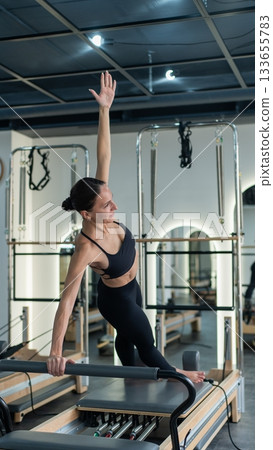 Caucasian woman doing side bends on reformer machine. Caucasian woman doing side bends on reformer machine. 133655783