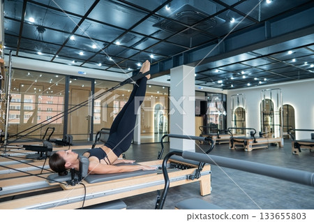 Caucasian woman doing exercises on reformer machine. Caucasian woman doing exercises on reformer machine. 133655803