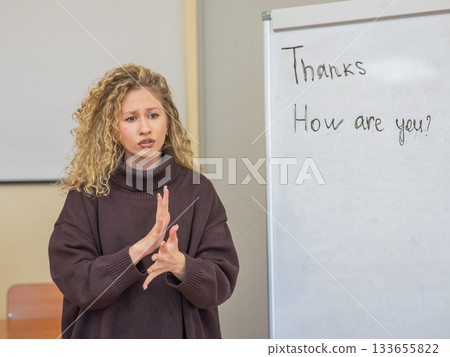 Caucasian female teacher communicates in Russian sign language with students. Caucasian female teacher communicates in Russian sign language with students. 133655822