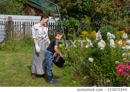Caucasian woman and her son watering flowers in the garden. Caucasian woman and her son watering flowers in the garden. 133655844