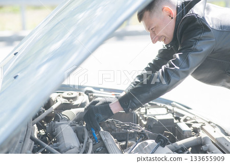 A man changes spark plugs in his car. A man changes spark plugs in his car. 133655909