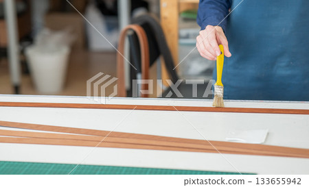 A craftsman uses a brush to cover leather parts. A craftsman uses a brush to cover leather parts. 133655942