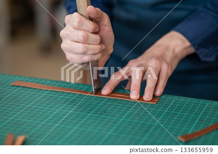 Woman tanner processes the edges of a leather belt in a workshop.  133655959