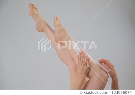 Woman applying moisturizer to her legs. White background. Woman applying moisturizer to her legs. White background. 133656074