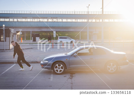 Caucasian man pulling a car with a rope. Caucasian man pulling a car with a rope. 133656118