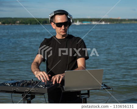 Male DJ playing music on the beach. Male DJ playing music on the beach. 133656131