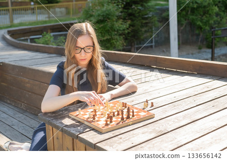 Caucasian woman playing chess outdoors. Caucasian woman playing chess outdoors. 133656142