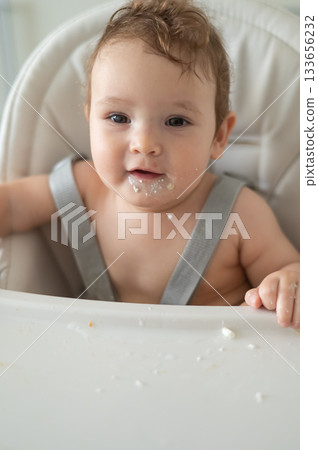 Cute baby boy smeared in sour cream sits in a high chair. Cute baby boy smeared in sour cream sits in a high chair. 133656232