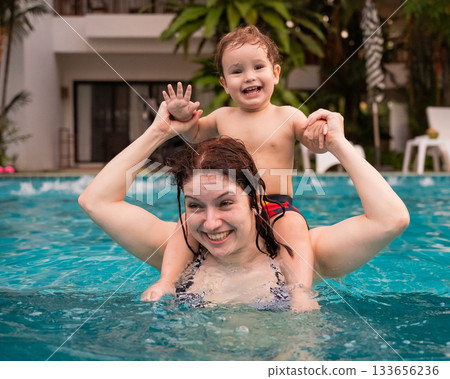 Caucasian woman holds her son while swimming in a pool on vacation. Mom teaches little boy to swim. Caucasian woman holds her son while swimming in a pool on vacation. Mom teaches little boy to swim. 133656236