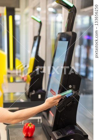 A woman pays using her smartphone at a self-checkout.  133656250