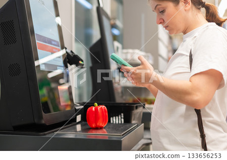 A woman buys bell peppers at a self-checkout.  133656253