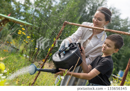 Caucasian woman and her son watering flowers in the garden. Caucasian woman and her son watering flowers in the garden. 133656345