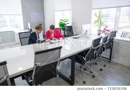 Man and woman talking while sitting at desk in office.  133656396