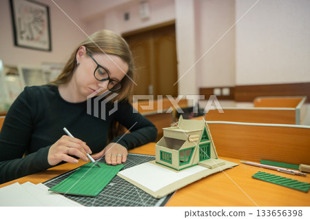 Caucasian young woman making a model of a building. Student of the construction university. Caucasian young woman making a model of a building. Student of the construction university. 133656398