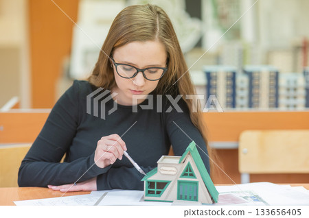 Caucasian young woman making a model of a building. Student of the construction university. Caucasian young woman making a model of a building. Student of the construction university. 133656405