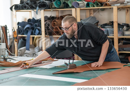 Caucasian bearded man working as a tanner in a workshop.  133656430
