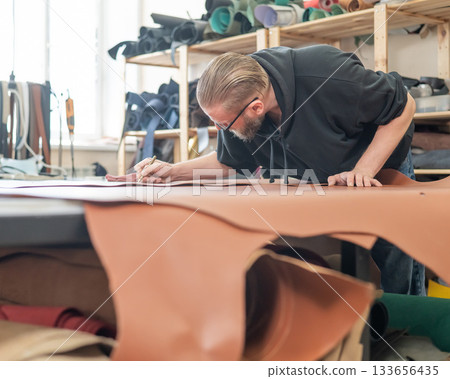 Caucasian bearded man working as a tanner in a workshop.  133656435