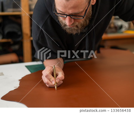 Caucasian bearded man working as a tanner in a workshop. Caucasian bearded man working as a tanner in a workshop. 133656438
