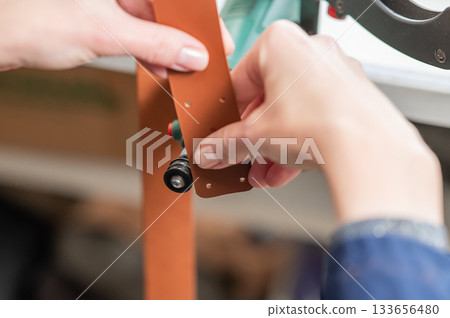 Leatherworker grinding the edge of a strip of leather for a belt in the workshop. Leatherworker grinding the edge of a strip of leather for a belt in the workshop. 133656480