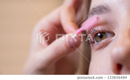 Caucasian woman brushing her eyelashes after lamination. Caucasian woman brushing her eyelashes after lamination. 133656494