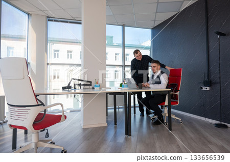 Caucasian man standing at colleague's desk discussing work.  133656539